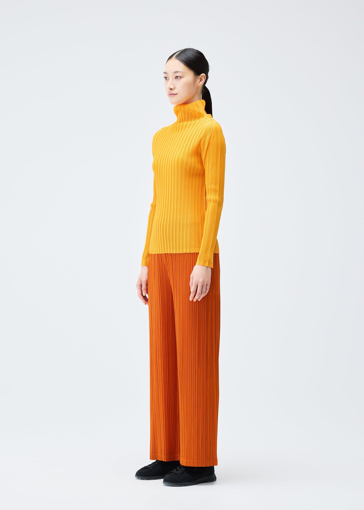 A model wears the Pleats Please Issey Miyake LOOP BOTTOMS trousers.