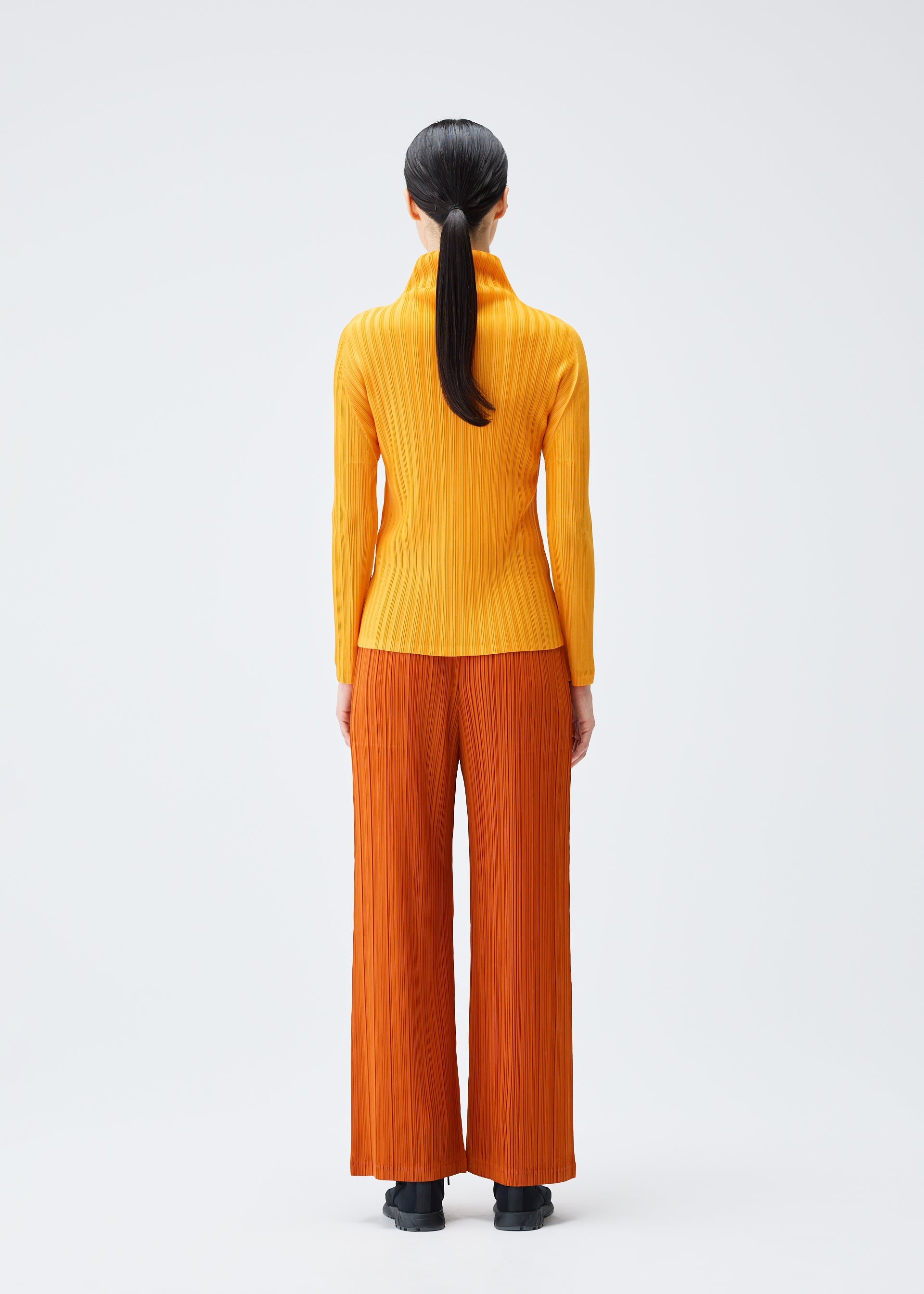 A model wears the Pleats Please Issey Miyake LOOP BOTTOMS trousers.