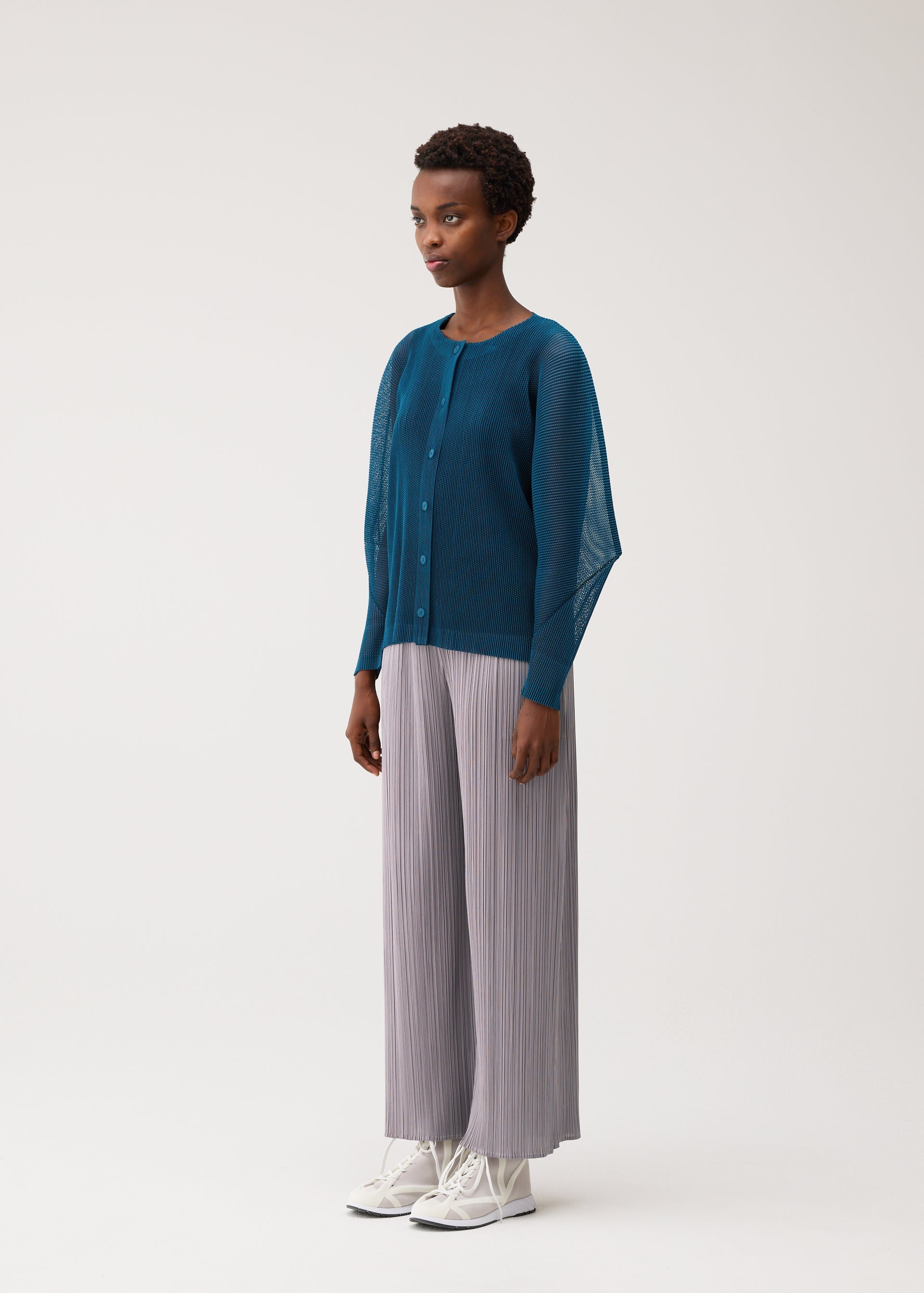 A model wears the PLEATS PLEASE ISSEY MIYAKE TATAMI AUGUST tatami-august-cardigan-greyish-green.