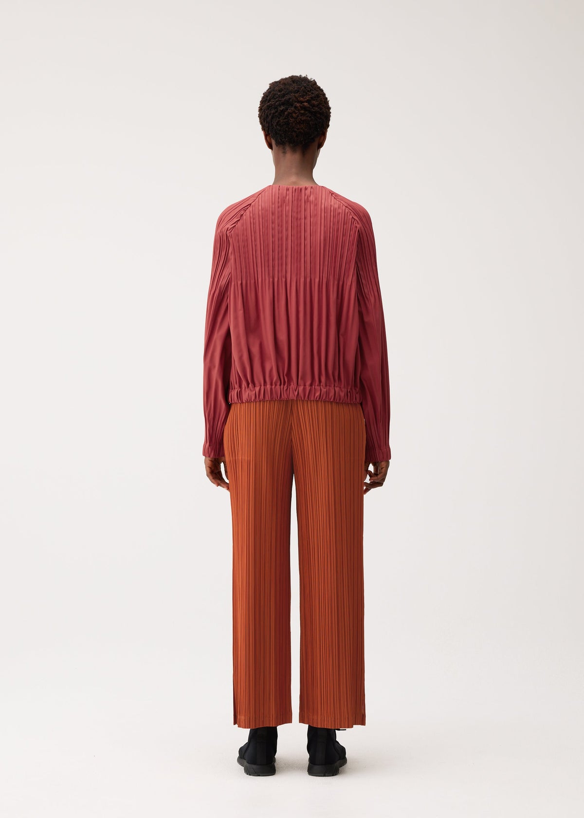 A model wears the PLEATS PLEASE ISSEY MIYAKE SMOOTH COAT coat.